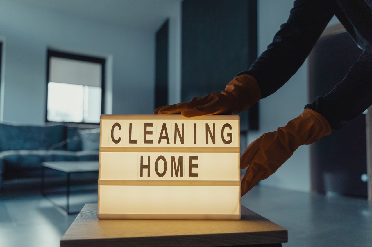 About Close-up of hands with rubber gloves holding an illuminated lightbox saying 'Cleaning Home'.